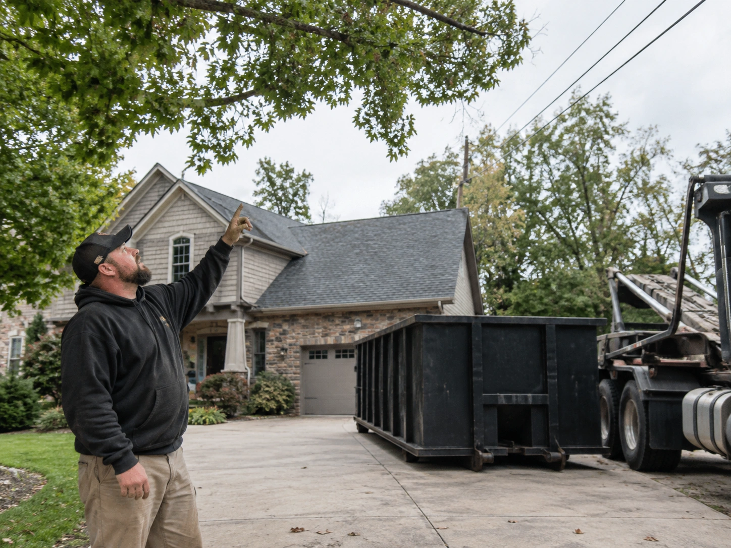 Delivery driver checking overhead tree branches and utility wires near a driveway placement area